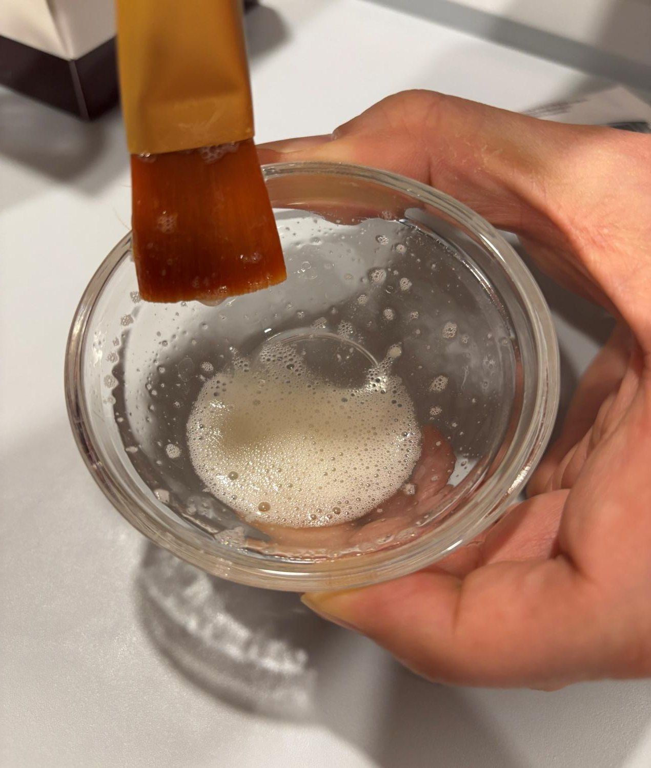 A brush lifting the mixed formulation from a glass bowl